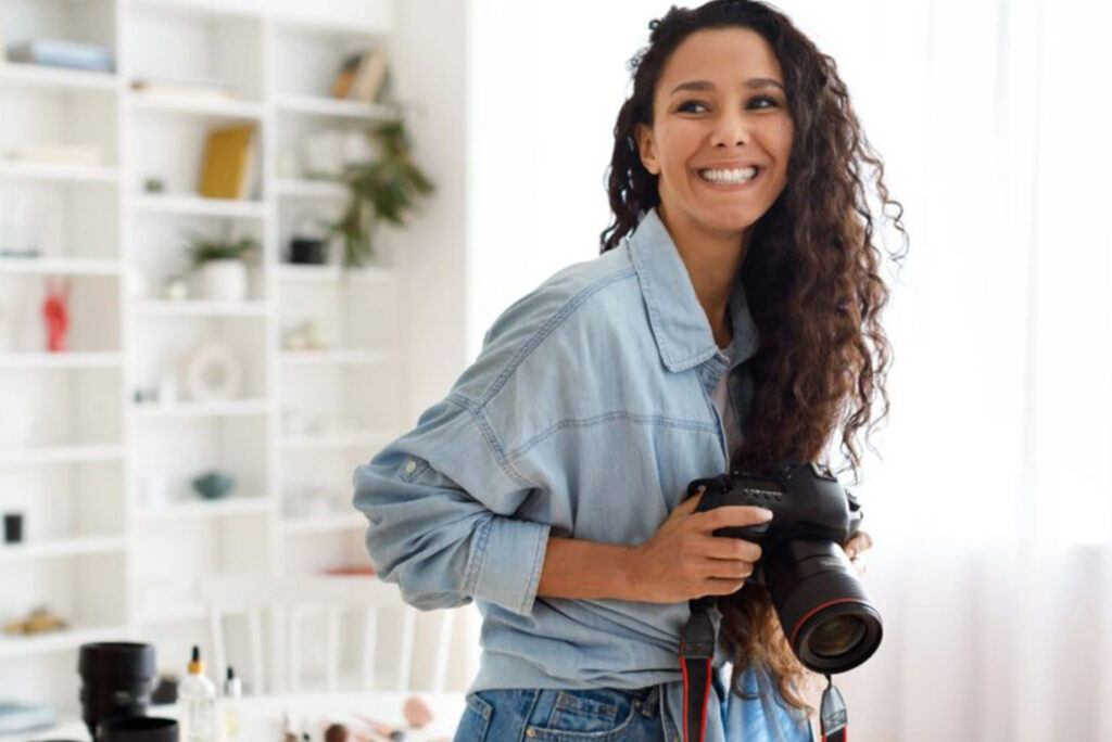 Smiling photographer holding a professional camera in a bright studio, symbolizing efficiency and organization when Choosing The Best CRM For Photographers.