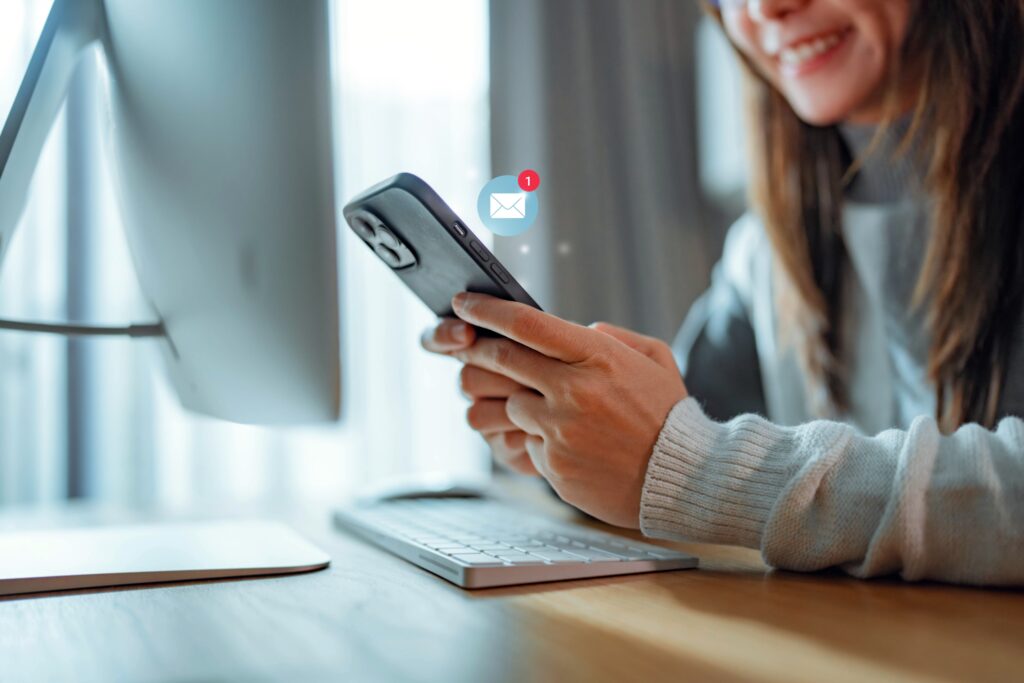 A person using a smartphone with a new email notification, sitting at a desk with a computer, showcasing email marketing for photographers ideas for success.