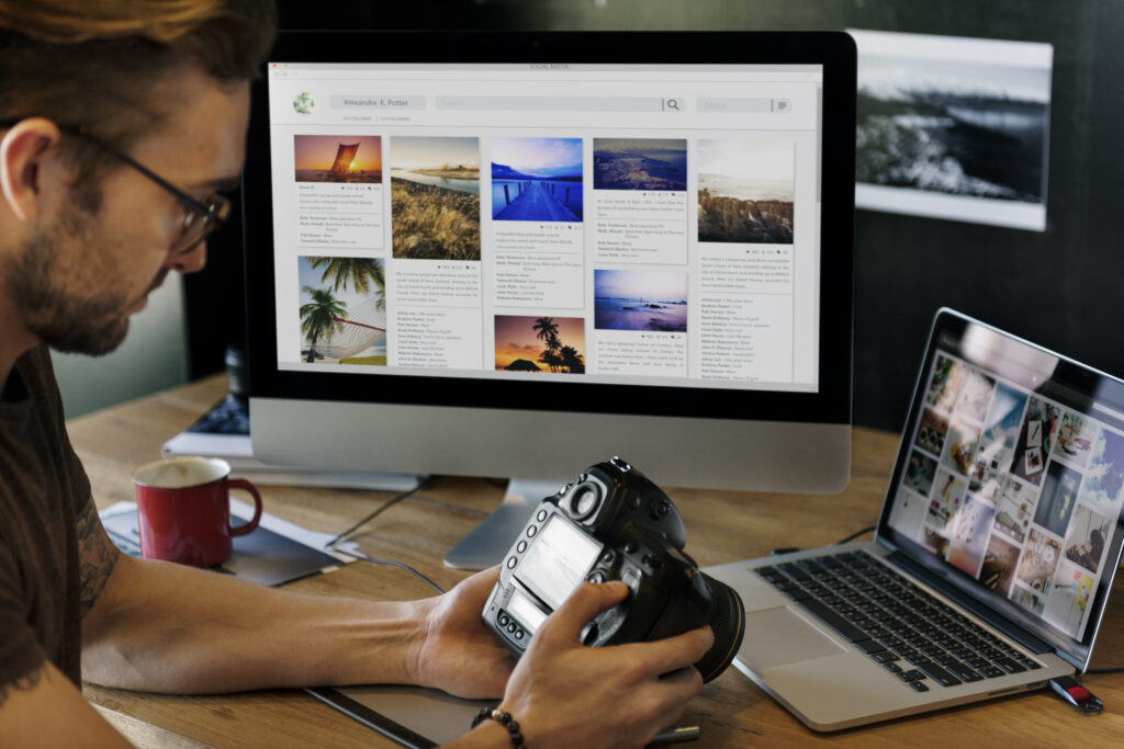 A photographer holding a camera while reviewing a social media portfolio on a computer and laptop, demonstrating how to become a well-known photographer through SEO, PR, and branding strategies.