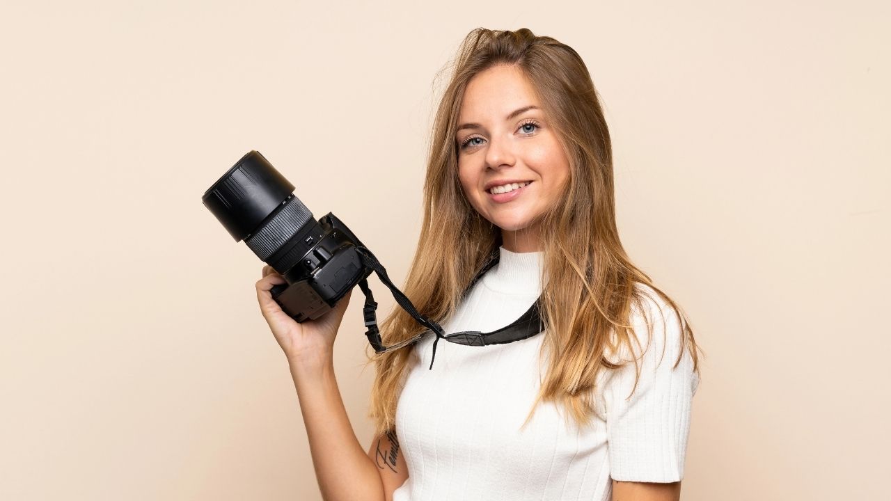 Smiling young woman photographer holding her camera, representing the benefits of photography mini sessions for growing business profits.