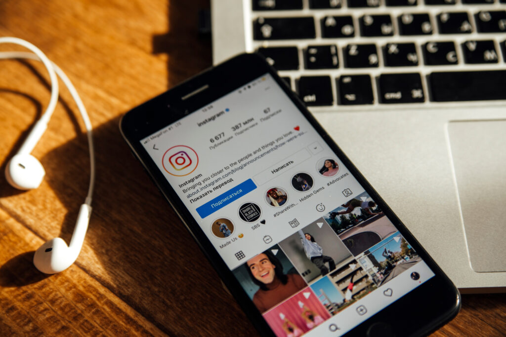 Close up of a Smartphone Showing an Instagram Profile Page Next to a Laptop and Earphones Illustrating Instagram for Photographers As a Platform to Connect with Clients