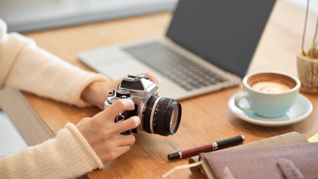 Photographer holding a camera at a desk with laptop and coffee, representing the question are Google Ads worth it for photographers when growing bookings.