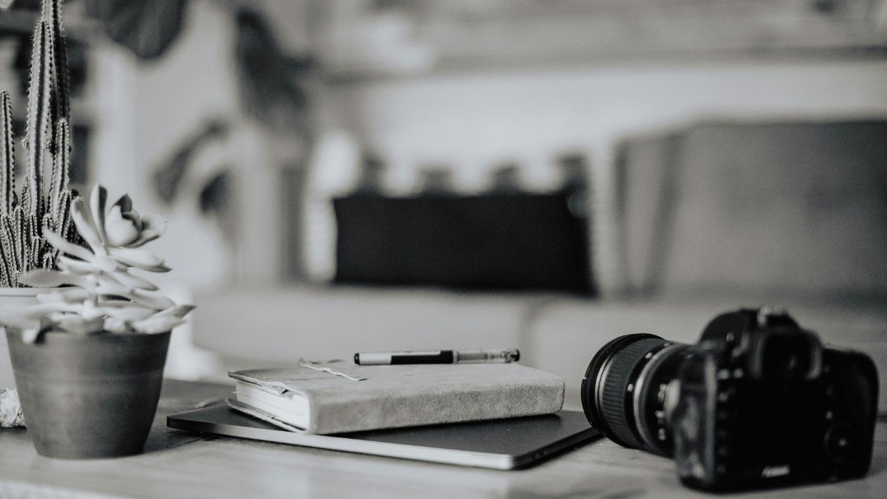 Camera placed on a desk beside a notebook and tablet, symbolizing planning and strategy for effective email marketing for photographers.