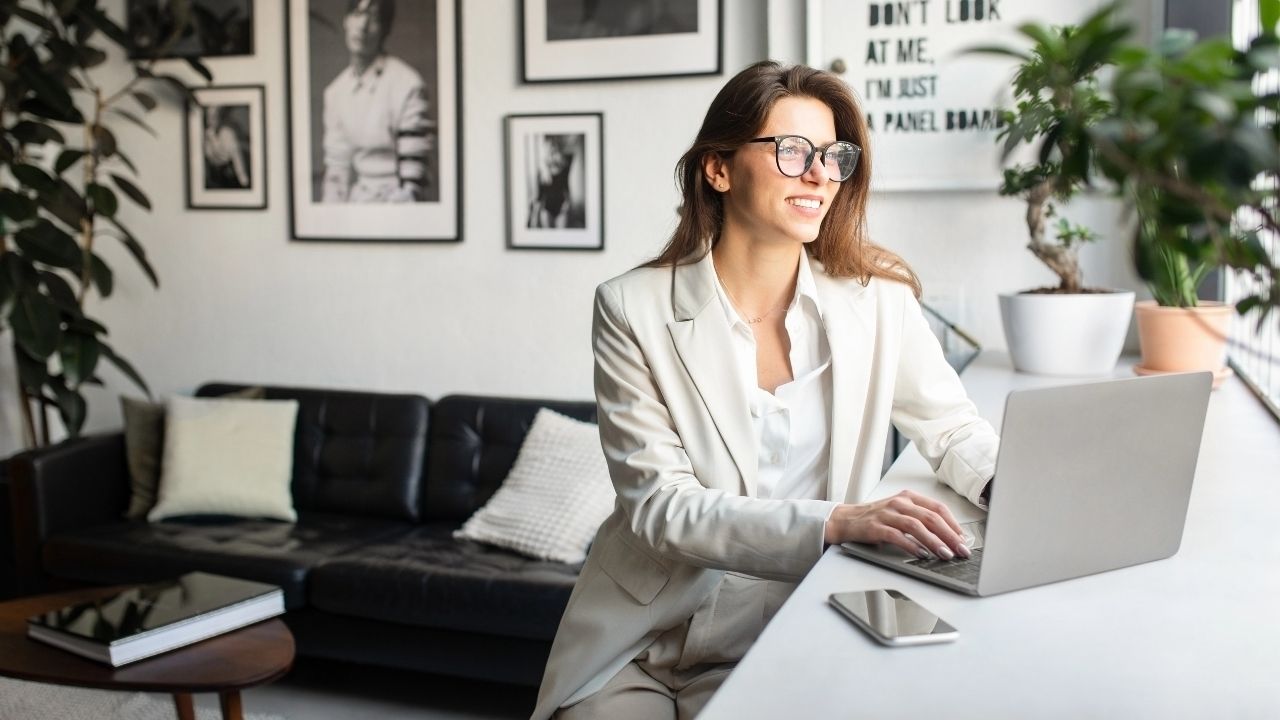 Smiling businesswoman working on a laptop in a modern office, representing how to advertise your photography business effectively online and offline.