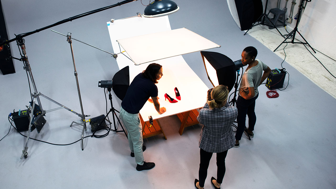 Professional photographers setting up a studio shoot with lighting equipment and red heels, illustrating how to get commercial photography clients through high-quality production work.