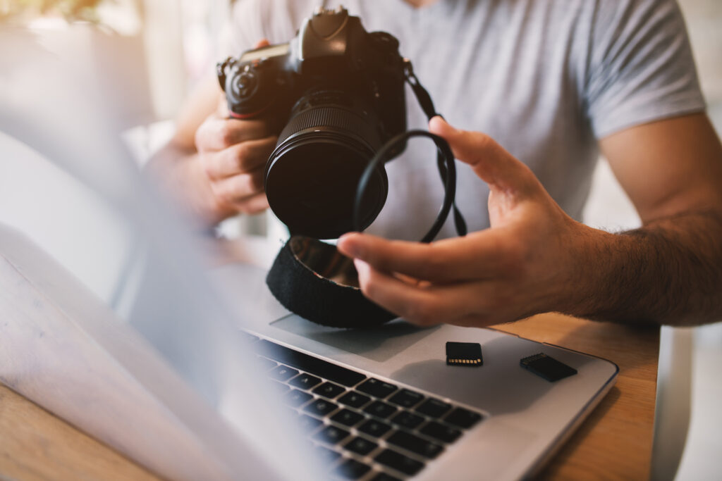Photographer holding a camera and lens filter over a laptop, symbolizing how reviews about photographers support professionalism and client trust.