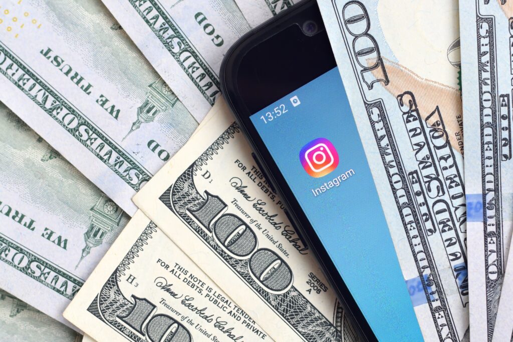 Smartphone with Instagram App Displayed on Screen Surrounded by Hundred dollar Bills Symbolizing Instagram for Photographers As a Tool to Generate Income