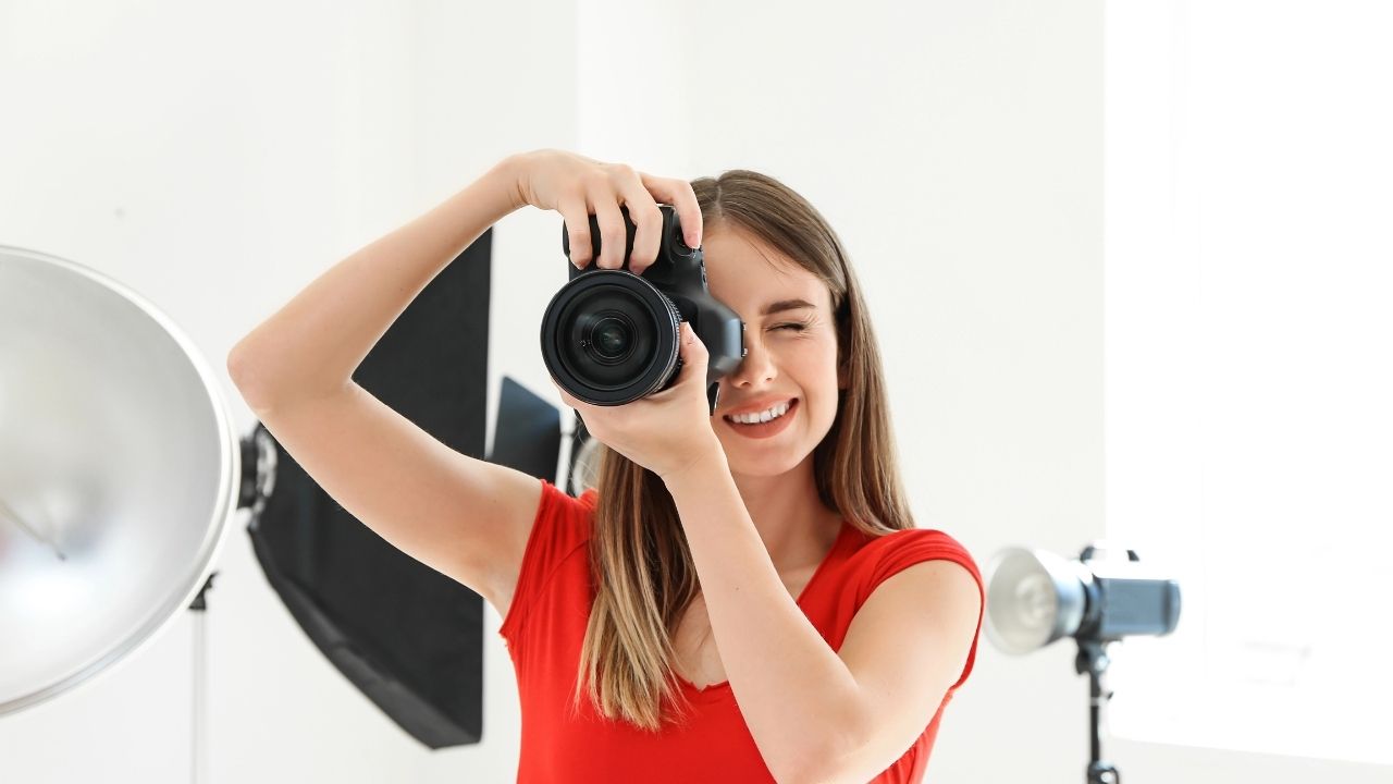 Smiling female photographer in a studio holding a camera, representing marketing blogs for photographers and how blogging helps attract more clients.