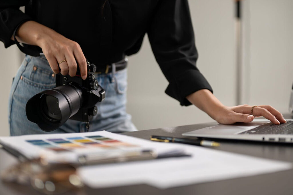 Photographer holding a camera while working on a laptop, symbolizing PR for senior photographers managing both creative work and brand promotion.