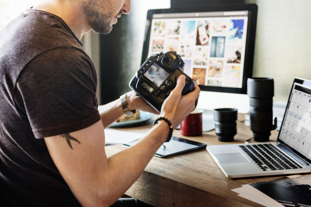 Photographer reviewing camera and digital portfolio at desk, representing where to advertise photography services effectively online and offline.