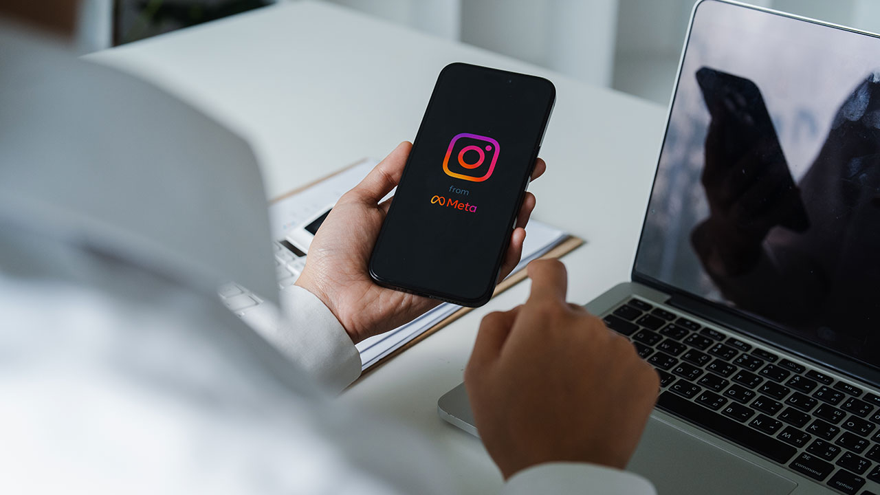 Person holding a smartphone with the Instagram app open next to a laptop, symbolizing the connection between PR and Instagram for photographers gaining premium clients.