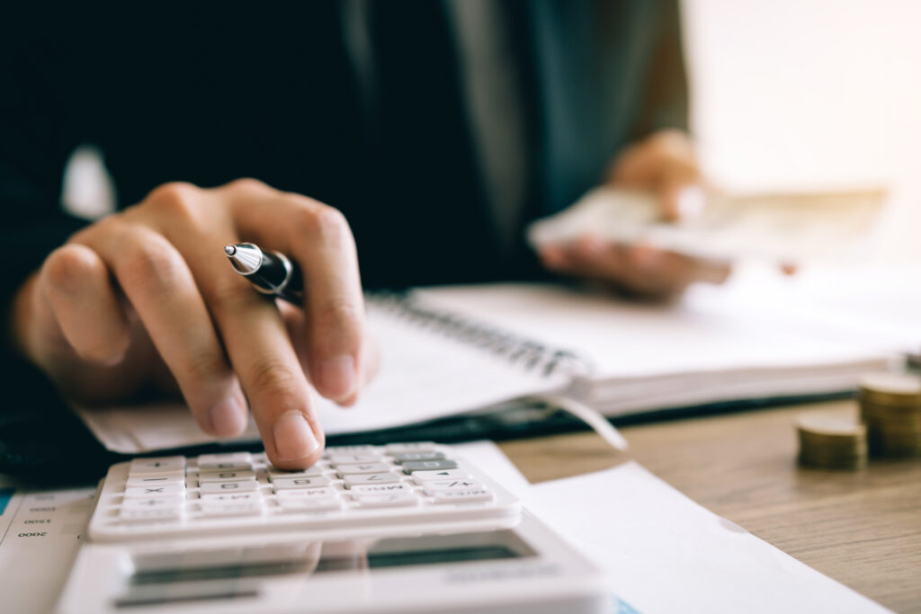 Close-up of a person calculating finances with coins and documents on a desk, representing the choice between marketing vs PR for photographers when growing a business.