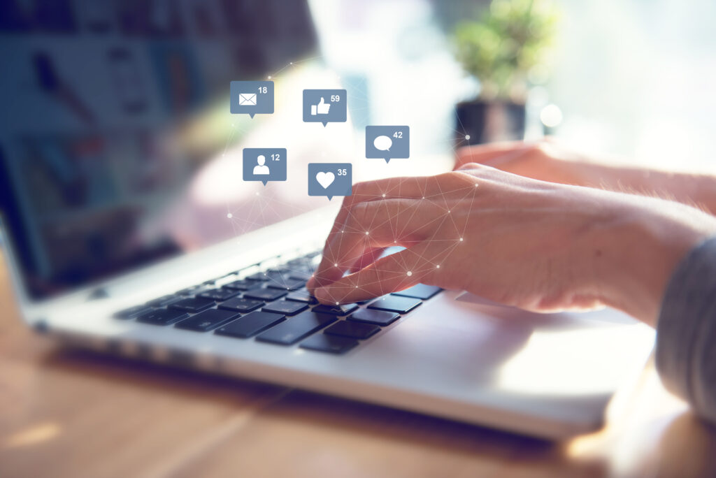 Hands Typing on a Laptop with Social Media Engagement Icons Symbolizing the Importance of Social Media for Photographers in Building Client Connections
