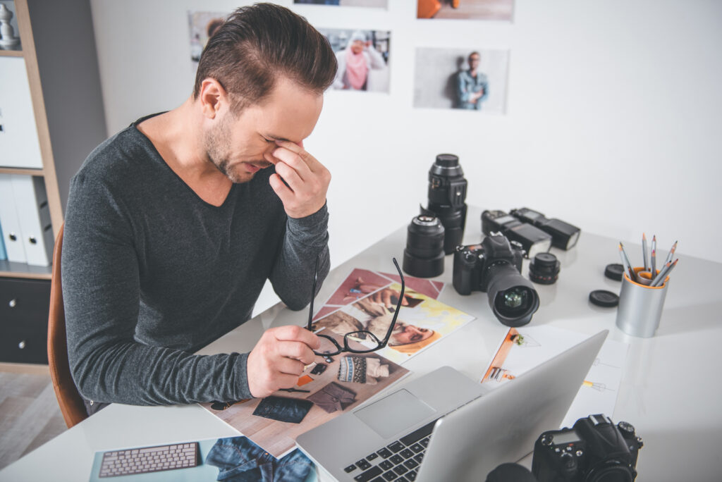 Frustrated photographer at desk with camera gear and laptop, representing challenges before using SEO for luxury photographers to attract high-value clients.
