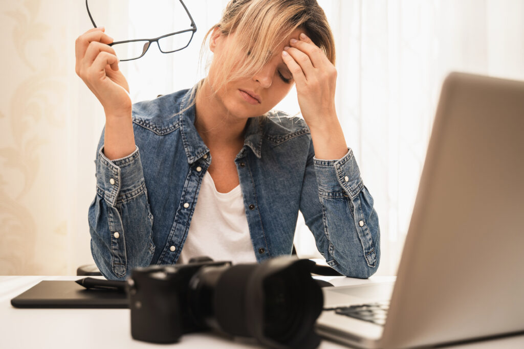 Stressed Photographer Sitting at a Desk with Camera and Laptop Reflecting the Challenges of Managing Social Media for Photographers