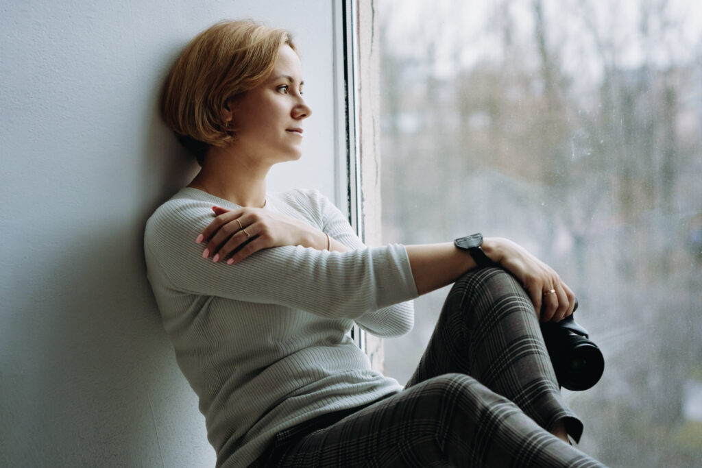 Female Photographer Sitting by a Window with Camera in Hand Representing Pr for Newborn Photographers Focused on Building Trust and Credibility