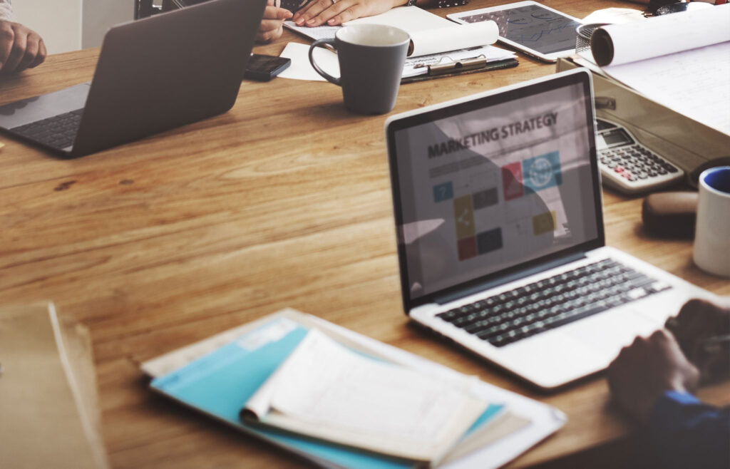 Open laptop showing a marketing strategy presentation on a desk with notebooks, coffee, and planners, representing marketing blogs for photographers to increase bookings.