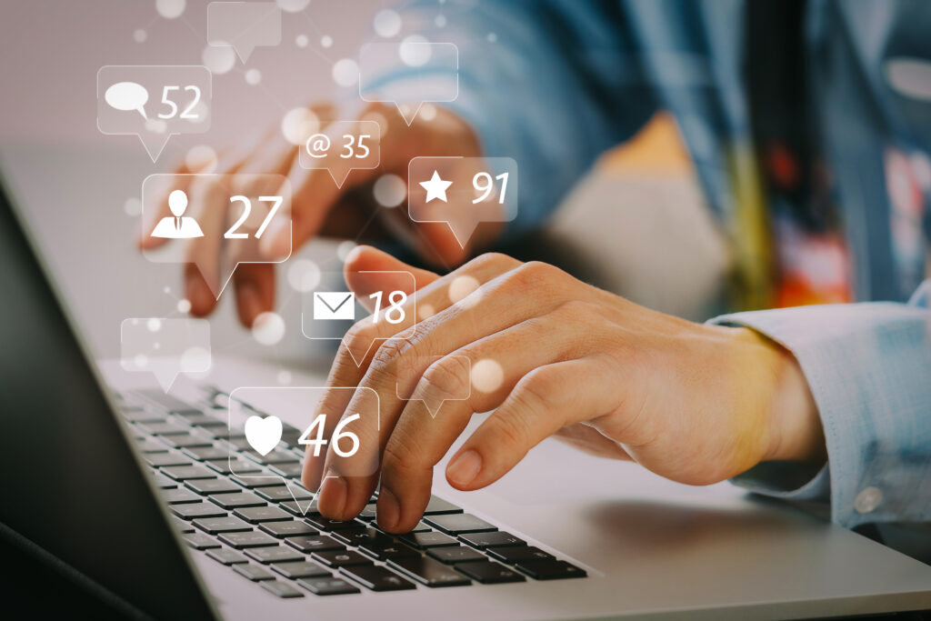 Hands typing on a laptop with social media engagement icons, illustrating Content Marketing for Photographers.